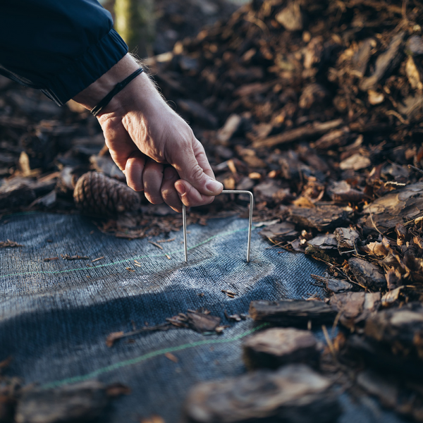 Galvanized weed mat peg being pushed through fabric with U-shaped staple