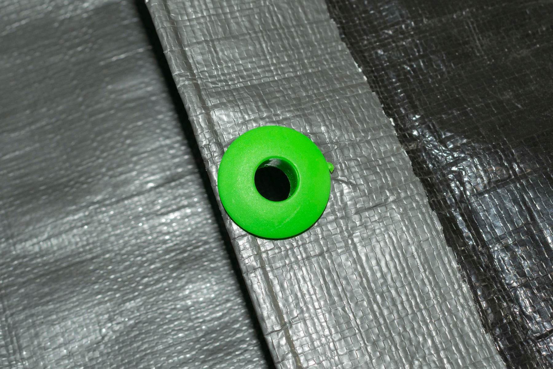 Green tarp eyelet fitted into gray tarpaulin fabric, ready to tie