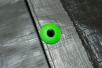 Green tarp eyelet fitted into gray tarpaulin fabric, ready to tie