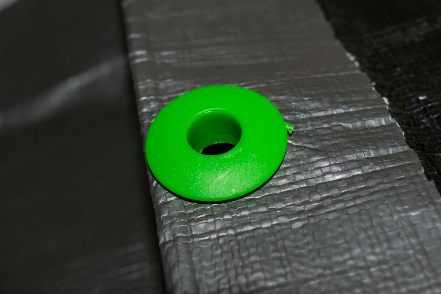 Single green tarp eyelet through gray tarpaulin, close-up