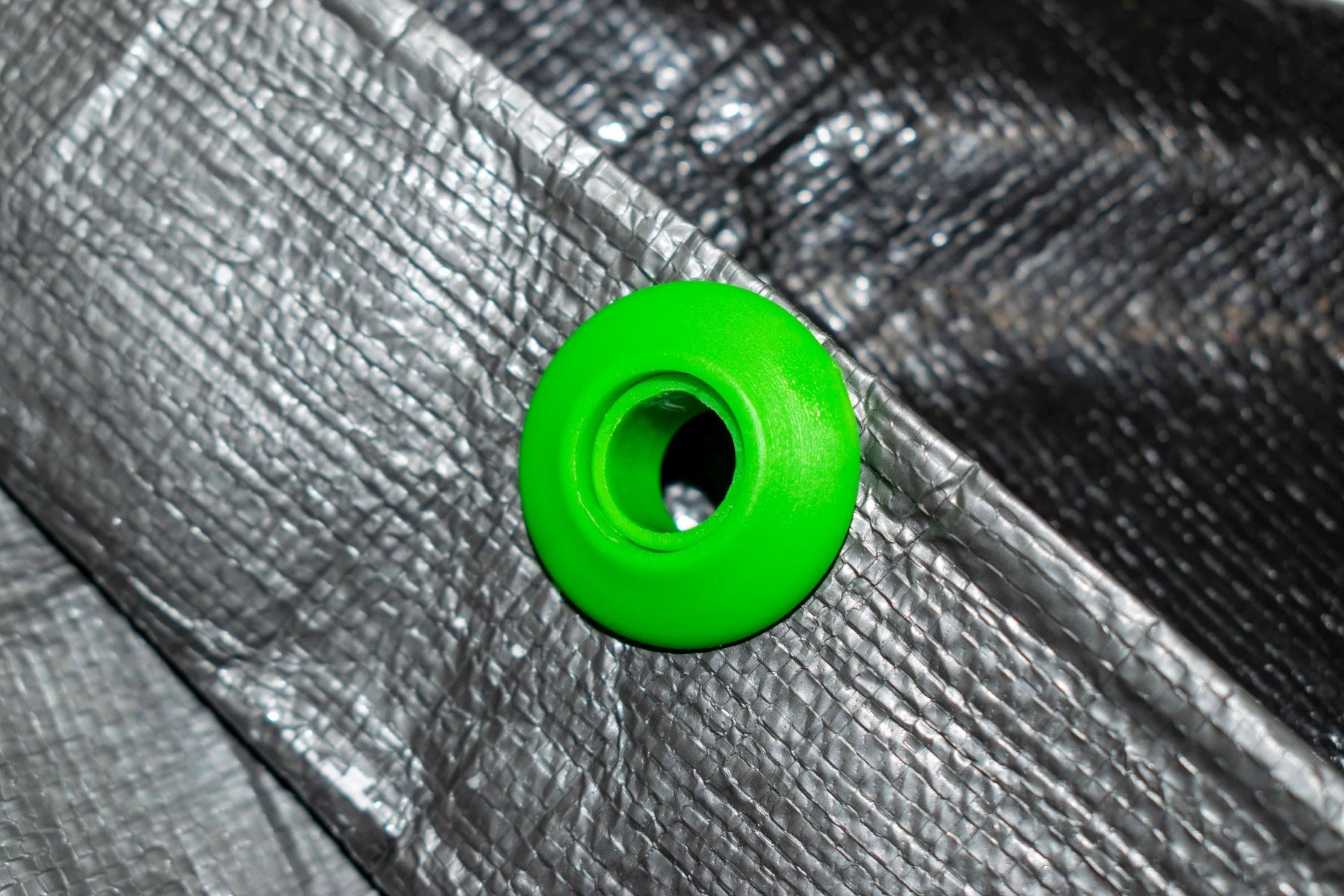 Single green tarp eyelet on metallic-looking tarpaulin, top view