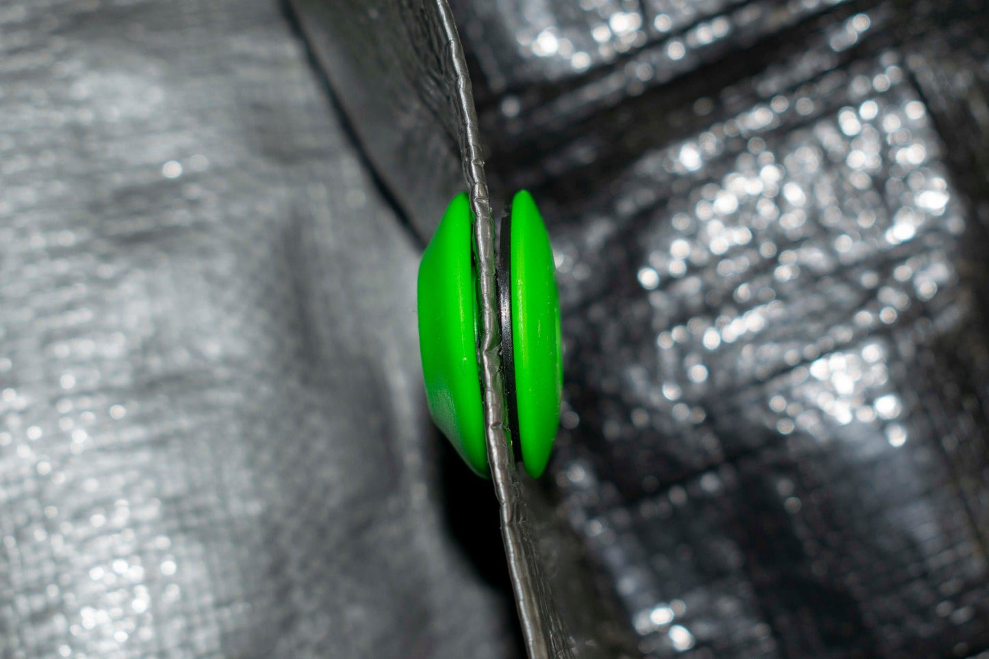 Side view of green tarp eyelet pressed into the tarp edge