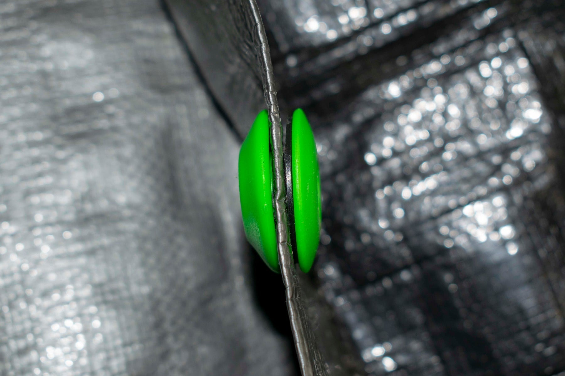 Side view of green tarp eyelet pressed into the tarp edge