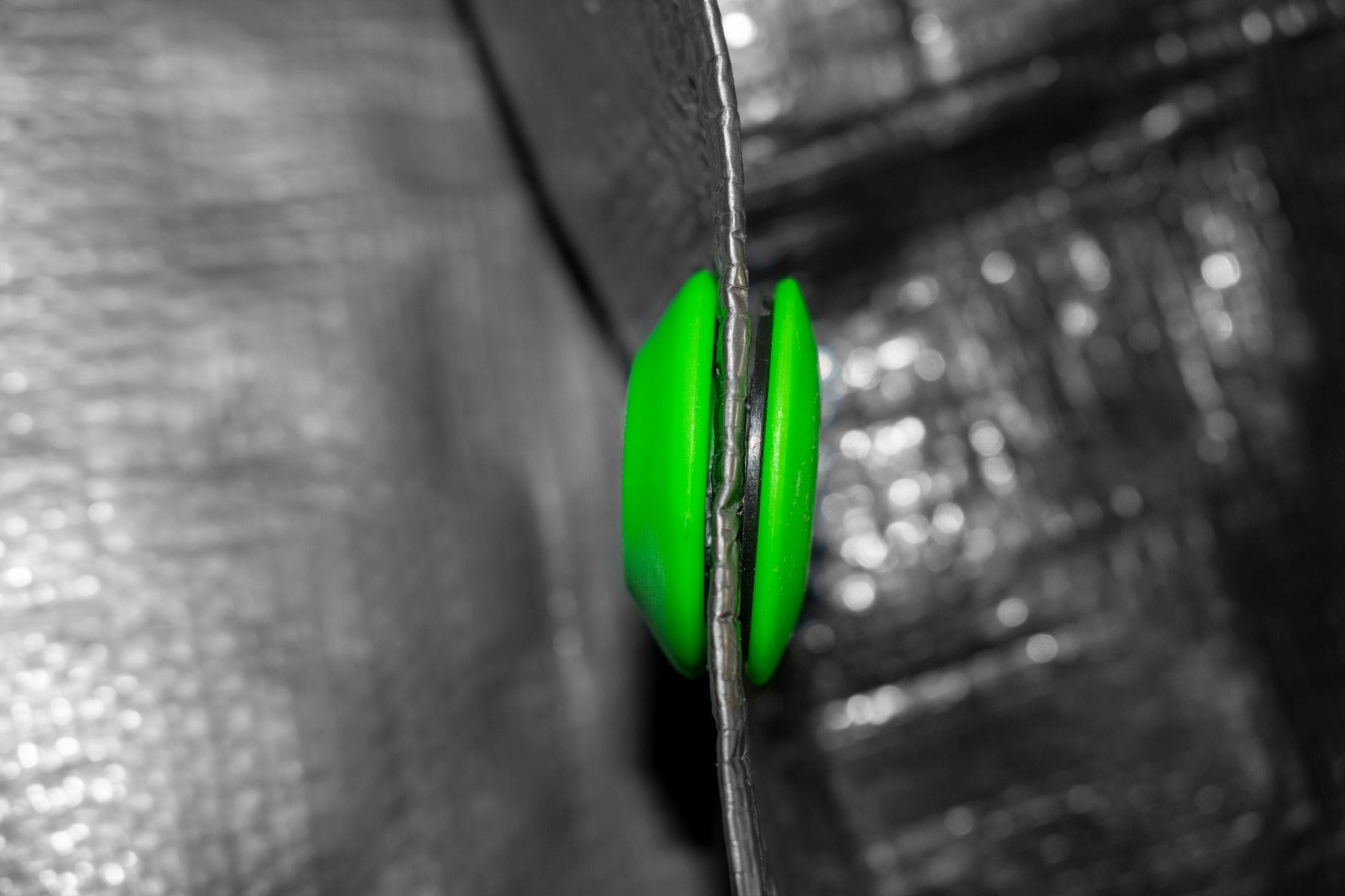 Green tarp eyelet through tarpaulin edge, side profile close-up