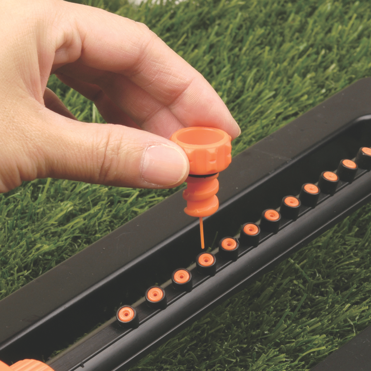Compact oscillating sprinkler head with orange nozzle, finger adjusting the jet holes bar