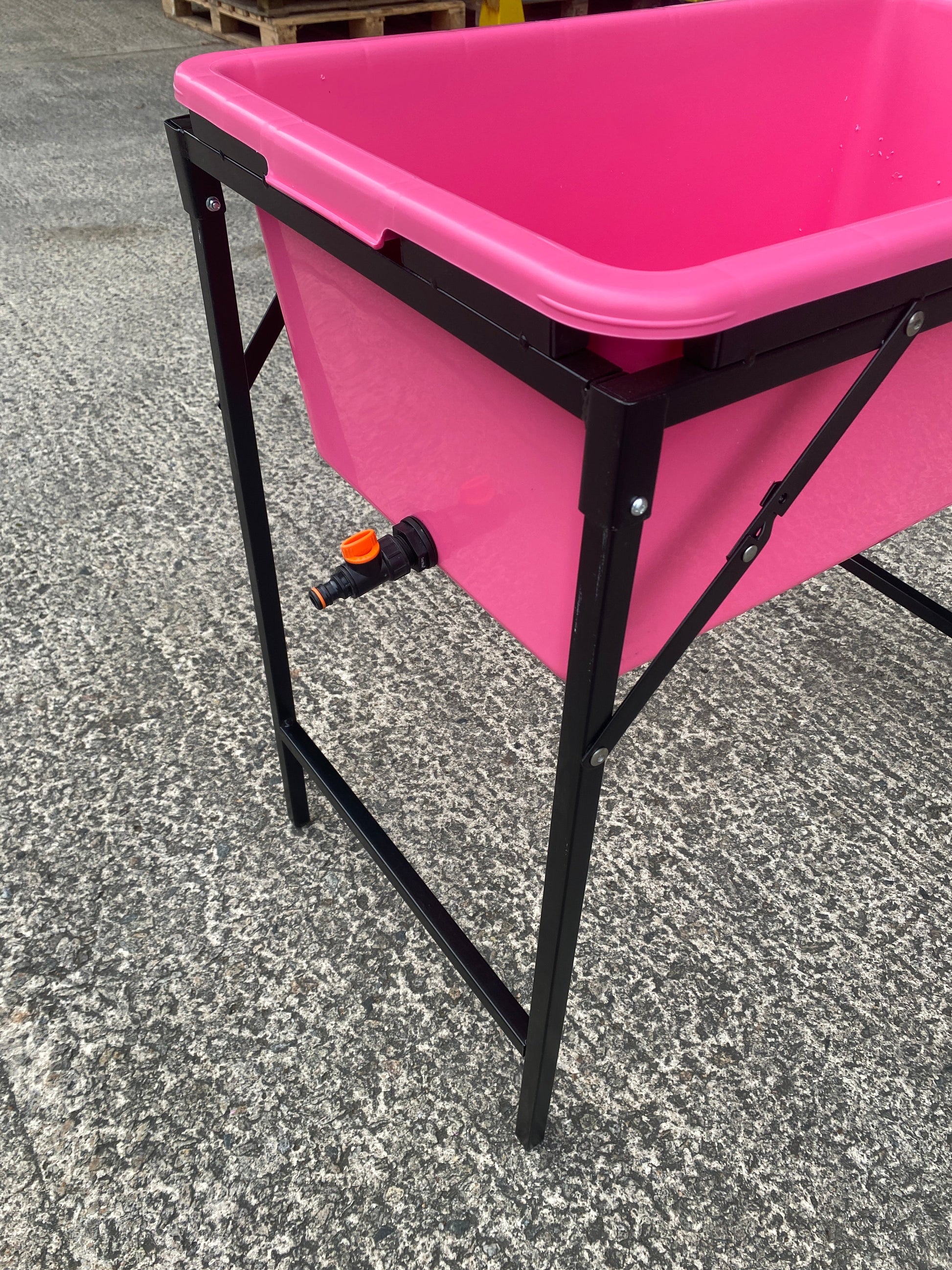 Pink dog bath with black stand and orange-handled drain valve at side
