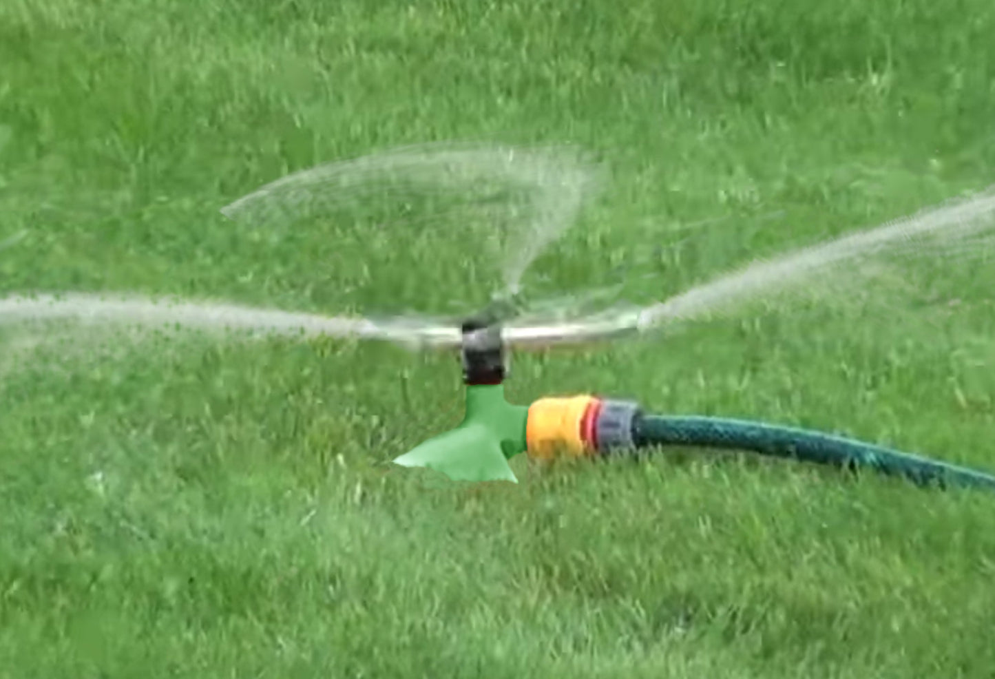 Green sprinkler running on lawn, water mist spraying from the brass head