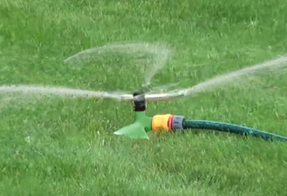 Green sprinkler running on lawn, water mist spraying from the brass head