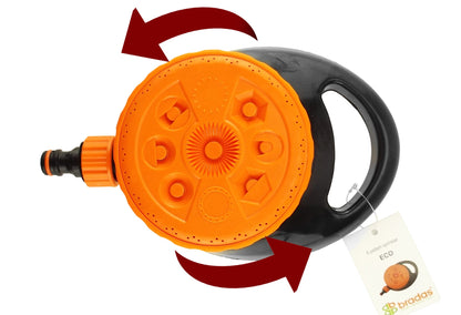 Static lawn sprinkler, orange top dial and black base with hose connector, showing spray pattern