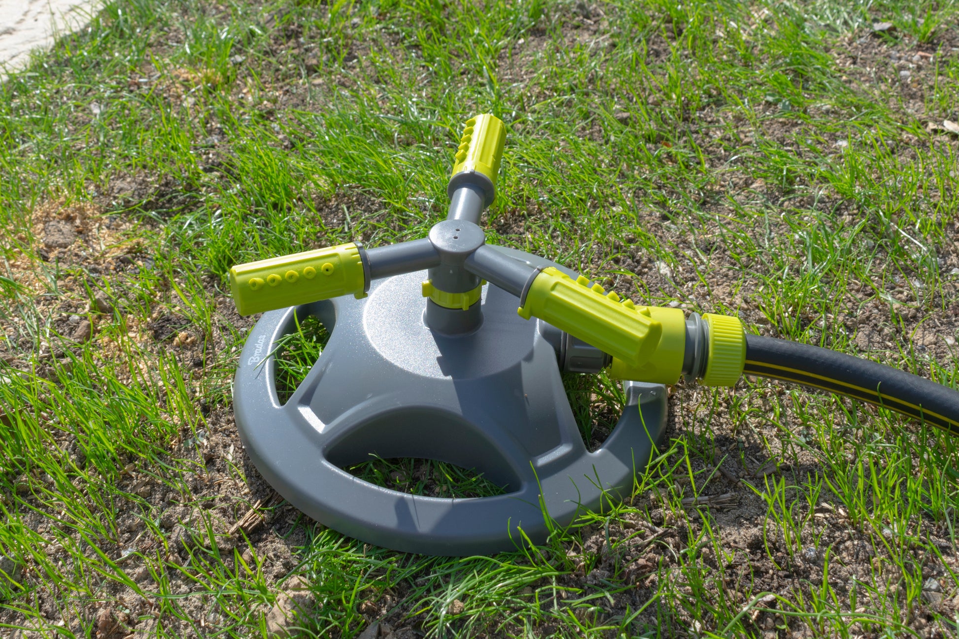 Rotating 3-arm sprinkler on grass, gray base with lime green spray arms
