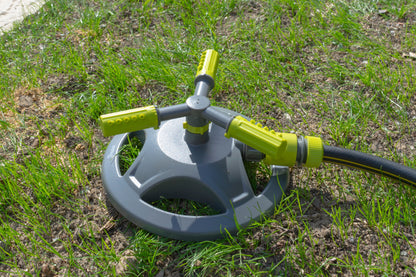 Rotating 3-arm sprinkler on grass, gray base with lime green spray arms